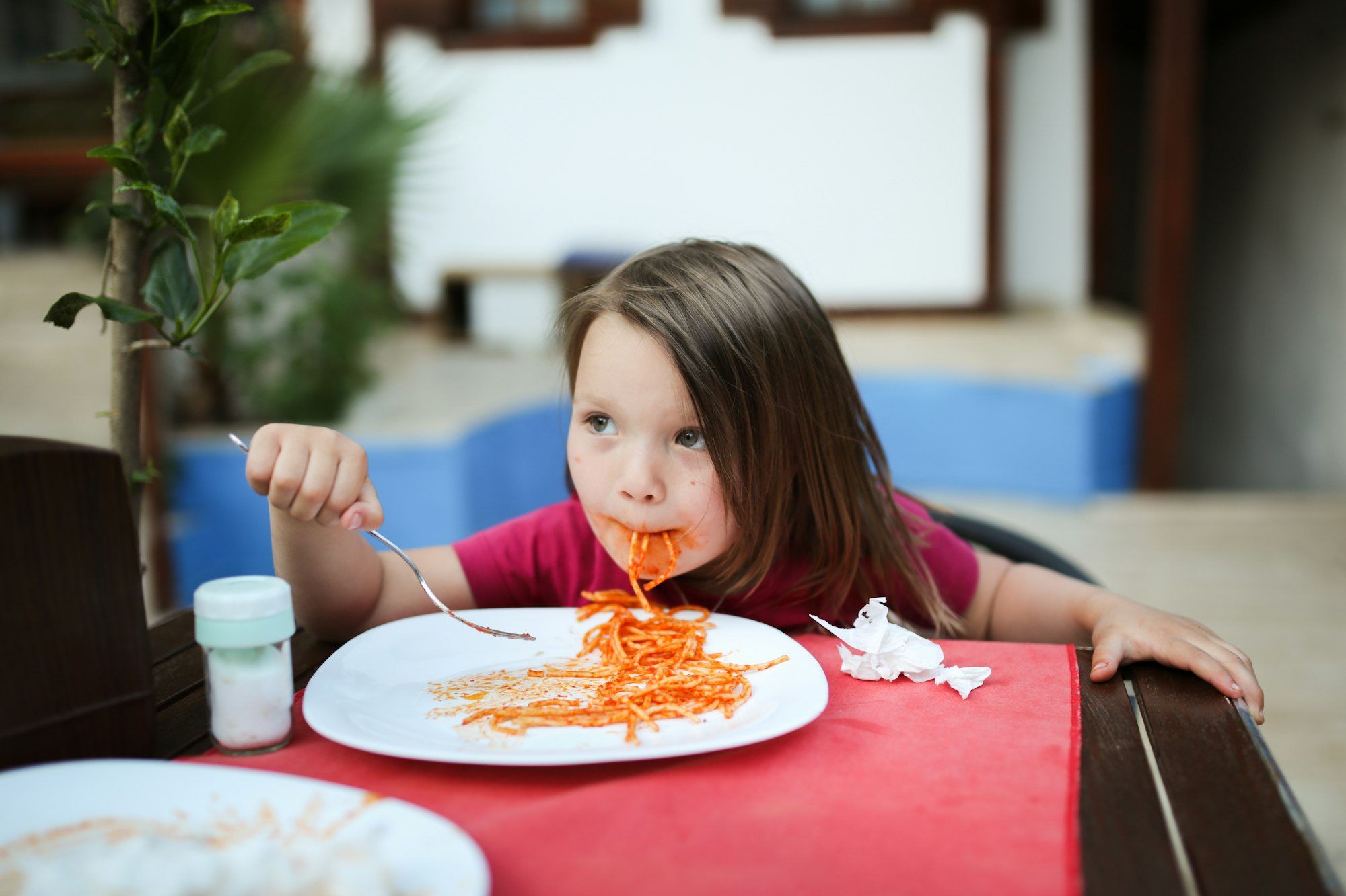 grimy girl child eats pasta with tomato sauce with a fork,