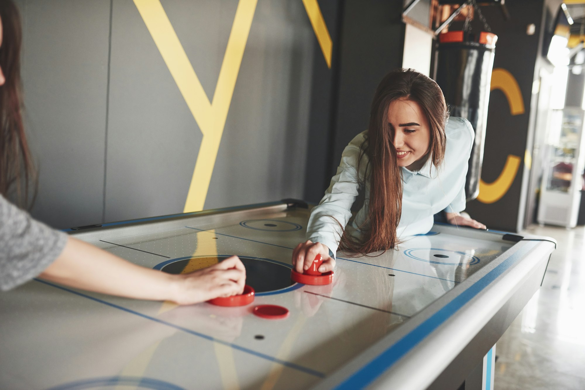 Two beautiful twin girls play air hockey in the game roomand have fun