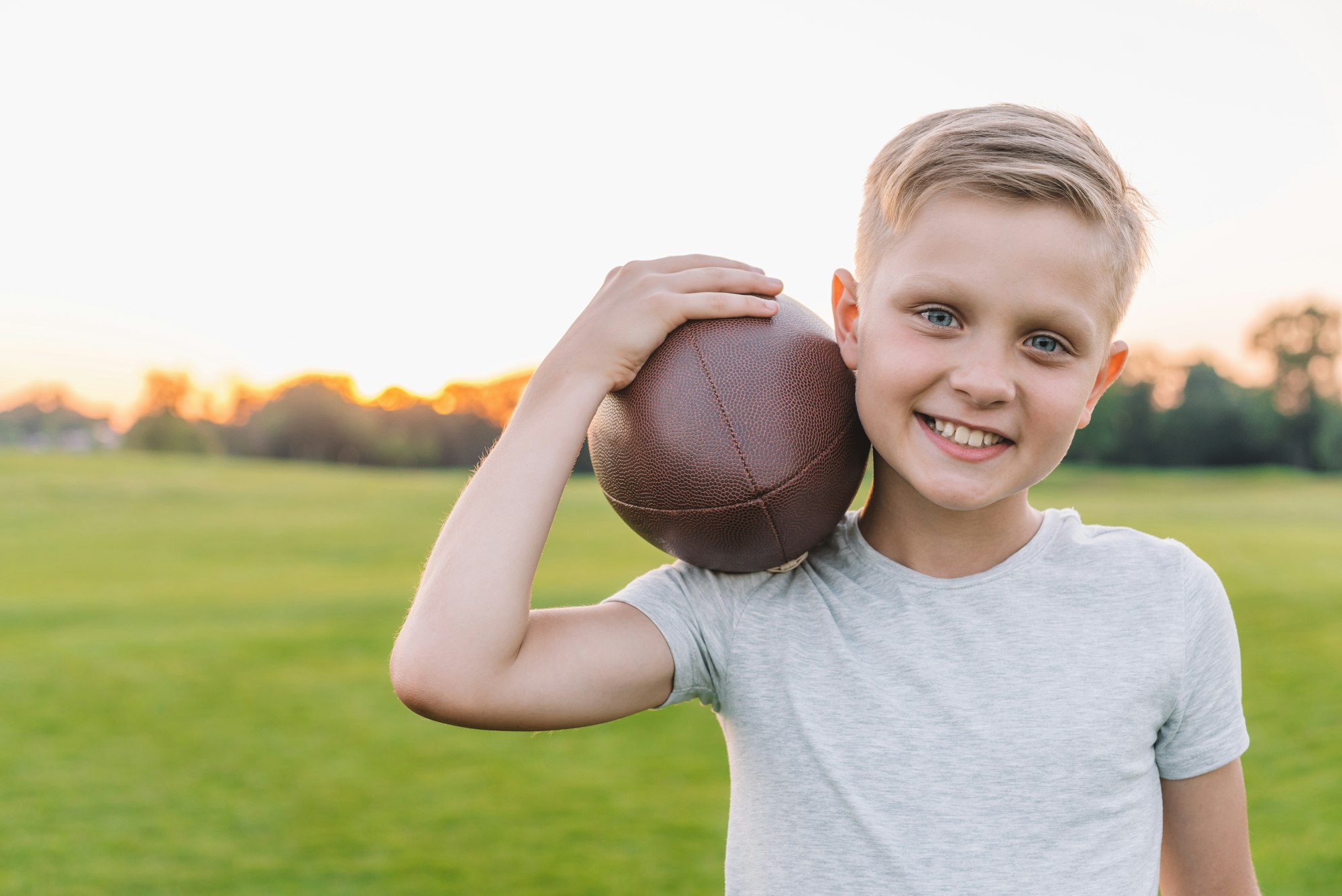 portrait of preteen boy holding rugby ball and looking at camera in park